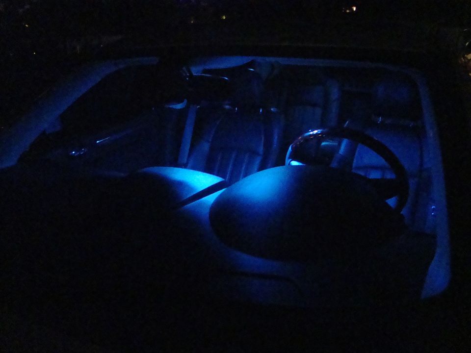 Car interior at night with blue LED ambient lighting illuminating the dashboard and seats