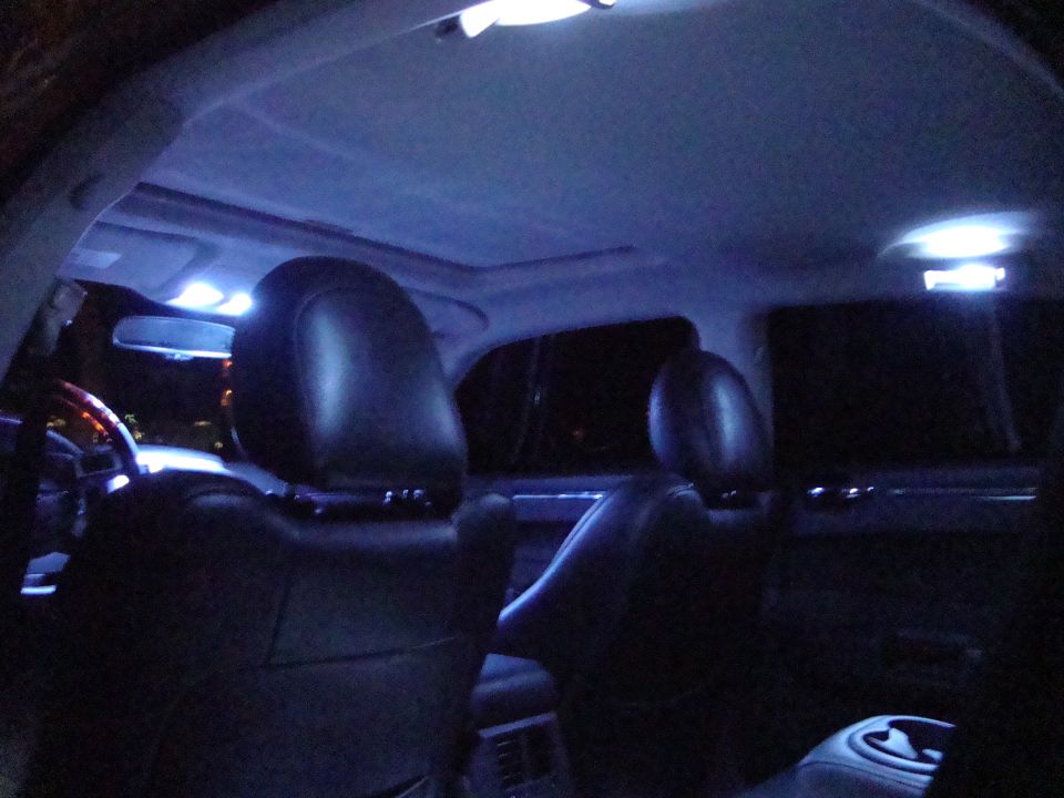 Sedan rear-seat view at night with white LED dome lights, sunroof and leather headrests