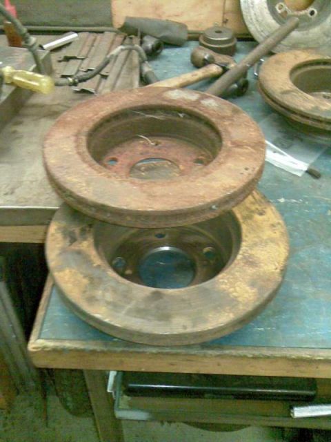 1969 MINI Cooper - Two heavily rusted brake rotors are shown on a workbench, suggesting they are parts for a vehicle repair or restoration project.