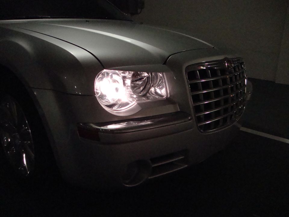 Silver Chrysler 300 front corner at night with headlight on and chrome grille