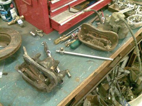 1969 MINI Cooper - A brake caliper and rotor are shown on a workbench, along with various tools and other automotive parts.