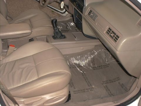 1995 Ford Taurus - The interior of a car shows tan leather seats and protective plastic floor coverings.
