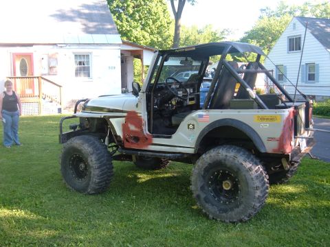 1976 Jeep CJ5 - Modified 1976 Jeep CJ5 parked on grass in front of a house, showing off its off-road tires and roll cage.