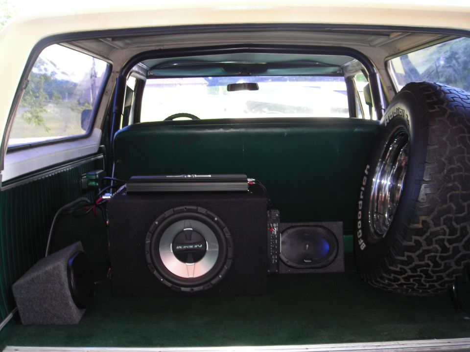 Interior view of a 1979 Ford Bronco showing aftermarket subwoofers, amplifier, and spare tire