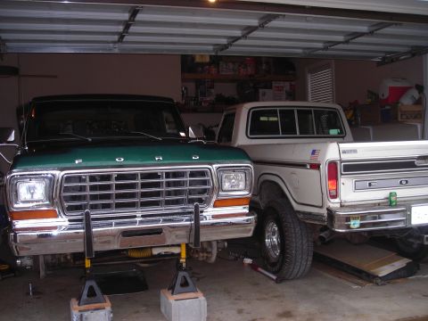 1979 Ford Bronco - Two Ford trucks are parked inside a garage, with the front truck on jack stands for maintenance.