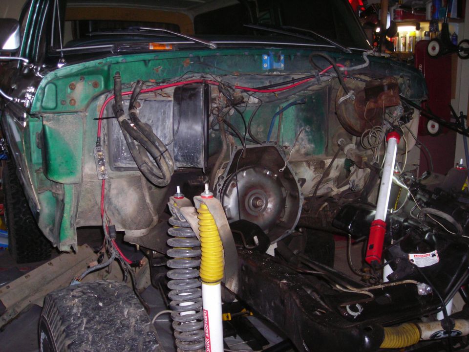 Green vehicle's engine bay is disassembled, showing the transmission and suspension components. Wires and hoses are exposed