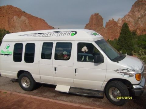 2006 Ford E250 - A white van with decorative decals and two dogs looking out the windows is parked outdoors with red rock formations in the background.