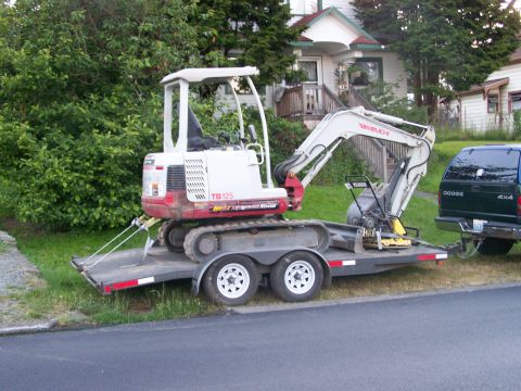 1988 Suzuki Samurai - A Takeuchi TB125 excavator is loaded onto a trailer, hitched to a Dodge 4x4 pickup truck.