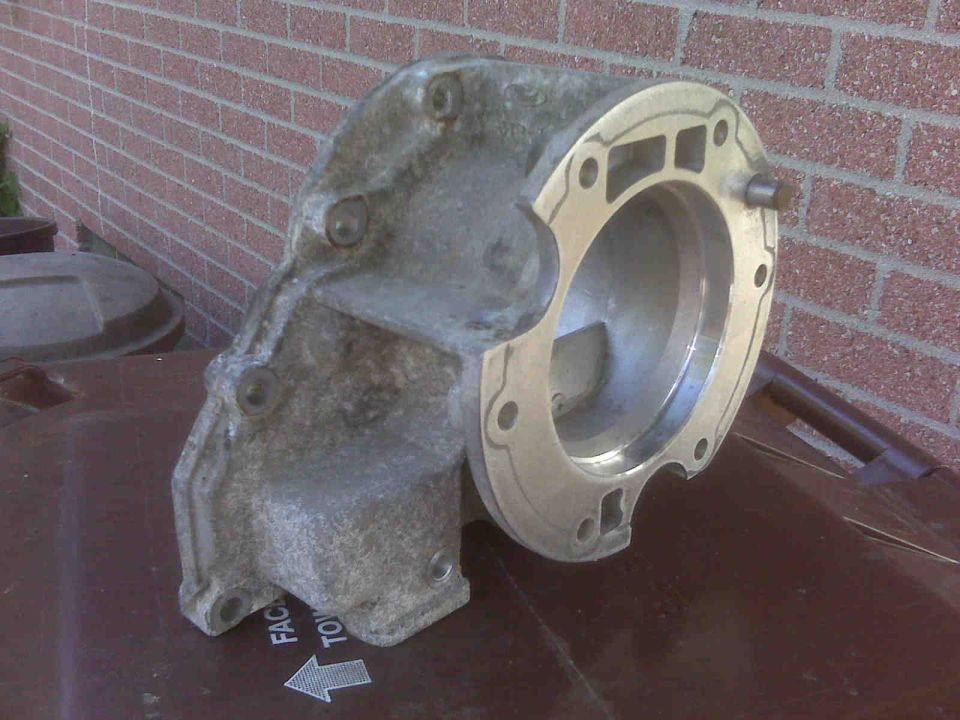 Aluminum automotive part with bolt holes and a circular opening, resting on a brown surface