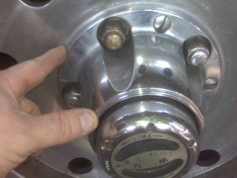 1995 Ford Bronco - A finger points to the edge of a chrome wheel hub assembly with a manual locking mechanism visible.
