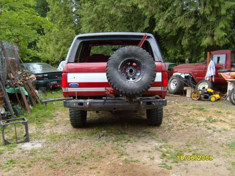 1989 Ford Bronco - Rear view of a 1989 Ford Bronco with a spare tire and custom bumper, parked outdoors with other vehicles.