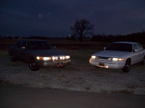 2000 Mercury Grand Marquis - Two sedans are parked side-by-side at night, illuminated by their headlights and auxiliary lights.