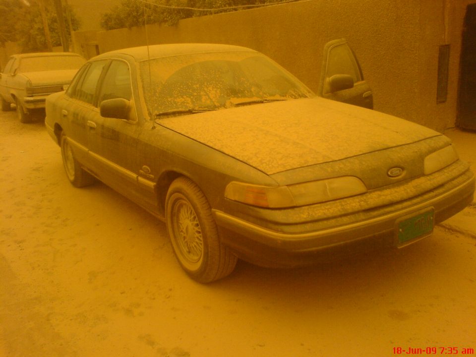 Dust-covered dark Ford Crown Victoria sedan parked in orange dust-storm light