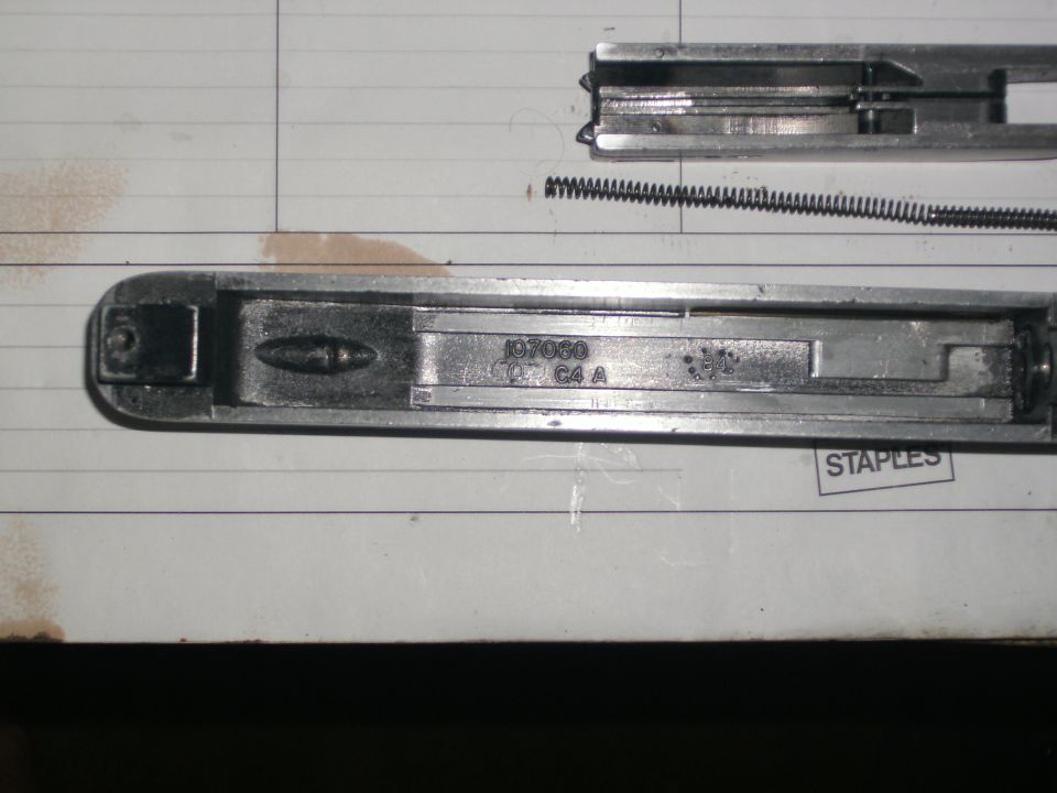 Close-up of a metal latch housing with stamped numbers and a spring