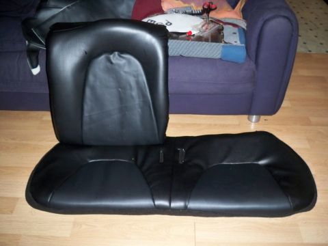 1995 Ford Probe - Black vinyl rear bench seat cushion and backrest laid on a wood floor near a couch.