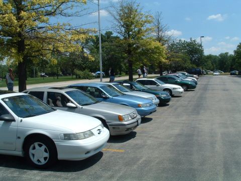 1993 Ford Taurus - A row of sedans, including a white 1993 Ford Taurus, are parked in a lot on a sunny day.