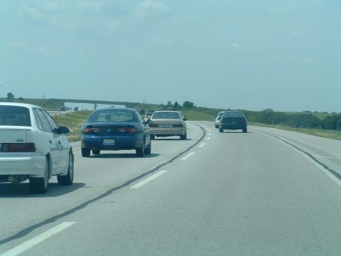 1993 Ford Taurus - Multiple vehicles travel along a highway on a partly cloudy day.