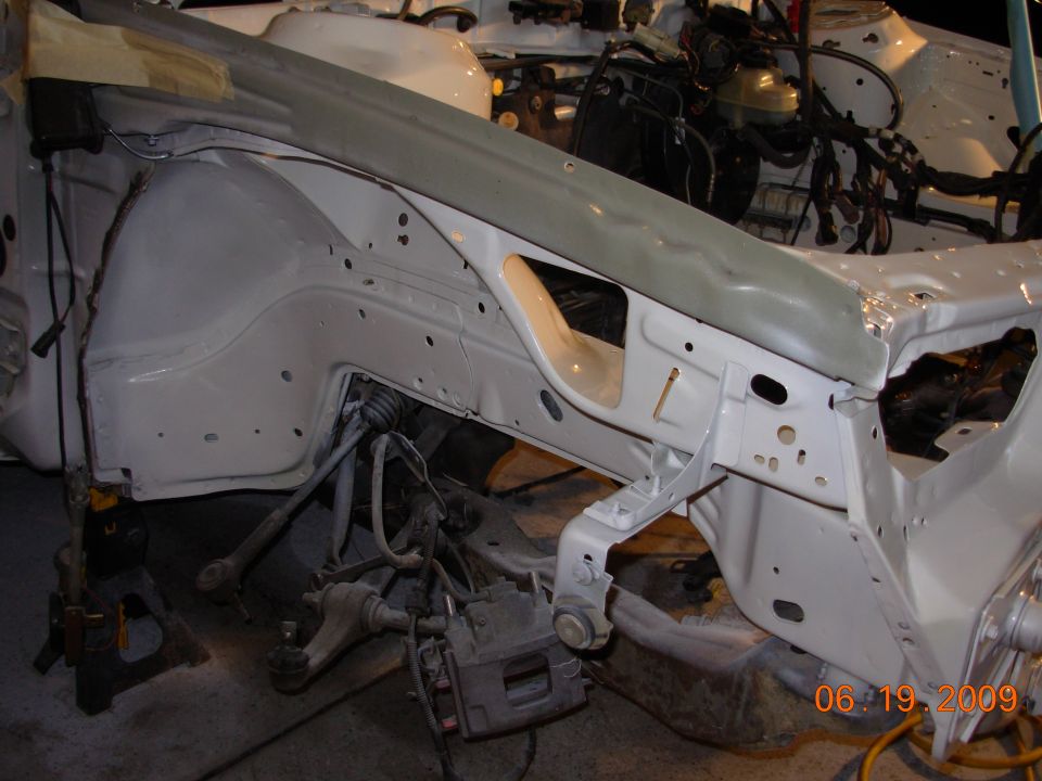 car's front wheel well area, suspension components visible, white paint