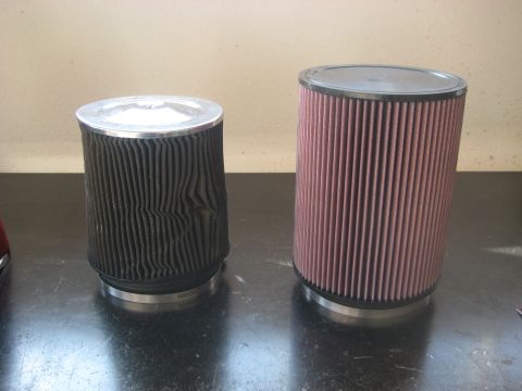 1996 Ford Bronco - A damaged black air filter sits next to a new pink air filter, both with metal tops and bases.