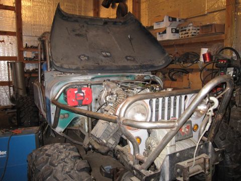 1992 Ford Bronco - This modified Jeep CJ-5 is undergoing work in a garage, with its hood open to reveal the engine and custom roll cage.