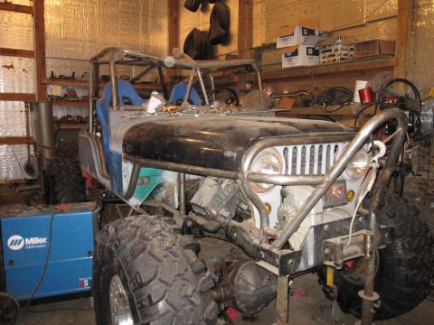 1992 Ford Bronco - This heavily modified jeep is undergoing a custom build in a workshop setting, a roll cage and large off-road tires.