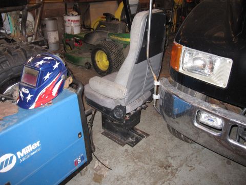 1992 Ford Bronco - A vehicle seat is positioned in front of a black truck's bumper, with a welding mask and machine nearby.