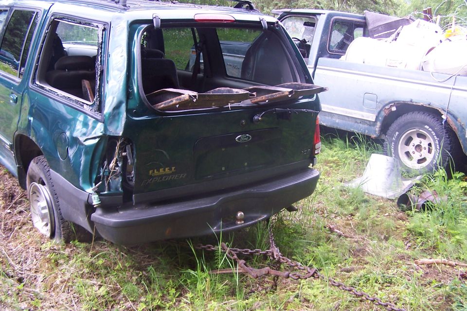 Green Ford Explorer with rear damage, broken windows, and a chain attached to the bumper