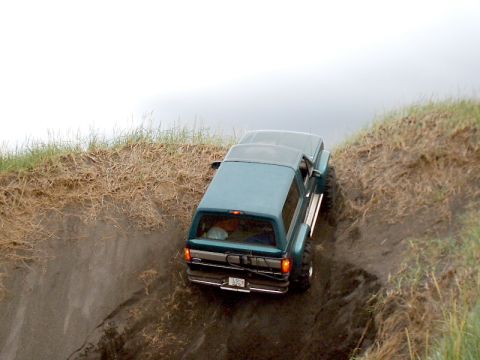 1996 Ford Bronco - A teal 1996 Ford Bronco navigates a steep dirt embankment from a rear perspective.