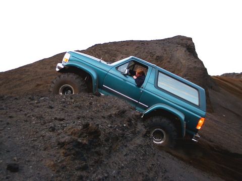 1996 Ford Bronco - Teal 2-door SUV navigates a challenging dirt incline, its off-road capabilities.