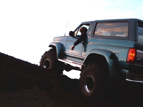 1996 Ford Bronco - A teal Ford Bronco with large tires navigates a steep dirt incline under a bright sky.