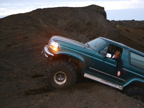 1996 Ford Bronco - A green SUV navigates a steep, dark dirt incline with a person visible inside.