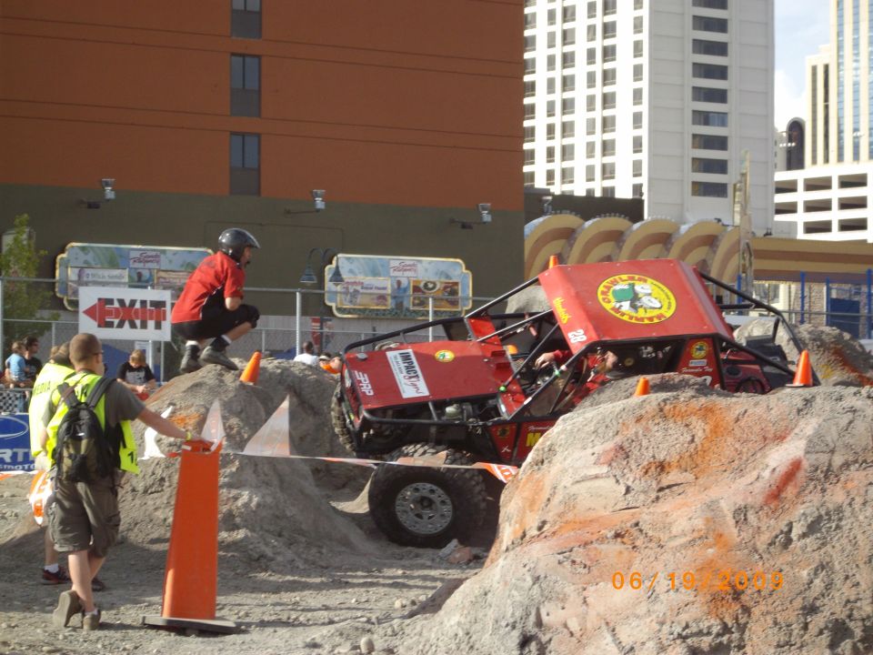 Red off-road buggy navigating a dirt obstacle course with spectators watching