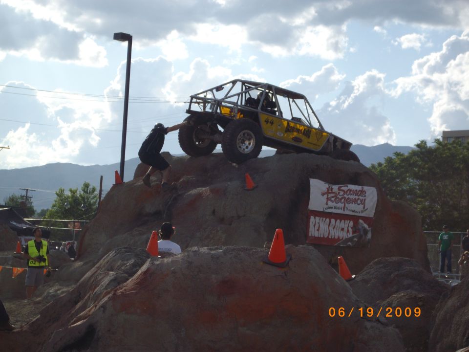 Yellow off-road buggy with roll cage climbing a rock obstacle, number 44 visible