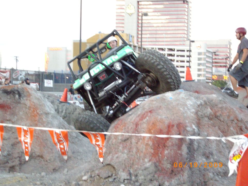 Off-road buggy with roll cage climbing over large rocks, driver wearing helmet