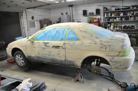 1996 Ford Bronco - A car is raised on jack stands in a workshop, undergoing body repairs and preparation for a new paint job.