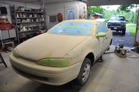 1996 Ford Bronco - Car body in primer, masked for painting, inside a garage with a truck outside.