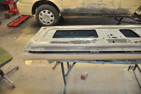 1996 Ford Bronco - A car tailgate with two window openings is shown, with a beige car undergoing repairs in the background.