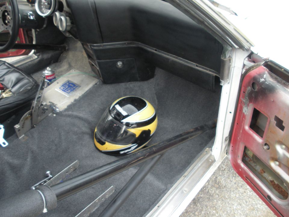 Car interior with racing helmet on floor, roll cage, and racing shifter