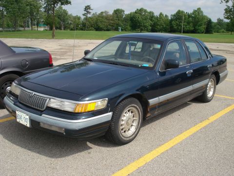2000 Ford Crown Victoria - A dark blue sedan, likely a Mercury Grand Marquis from the mid-1990s, is parked in a lot.