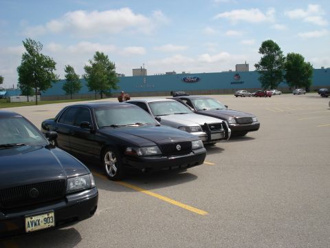 2000 Ford Crown Victoria - Several Ford Crown Victorias are parked in a lot with a factory building in the background.