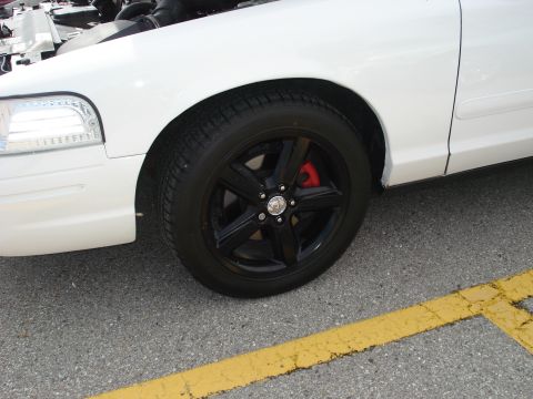 2000 Ford Crown Victoria - Close-up of a white sedan's front wheel and fender, showing a black wheel with red brake calipers.