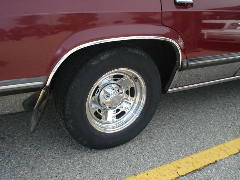 2000 Ford Crown Victoria - A close-up view of the rear wheel and fender of a dark red sedan, showing chrome accents and a mud flap.