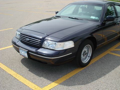 2000 Ford Crown Victoria - This dark blue 2000 Ford Crown Victoria is parked in a lot, showing its front quarter profile with distinctive chrome grille and wire wheel…