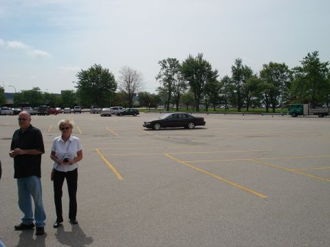 2000 Ford Crown Victoria - A dark sedan is parked in a large, mostly empty parking lot on a cloudy day.