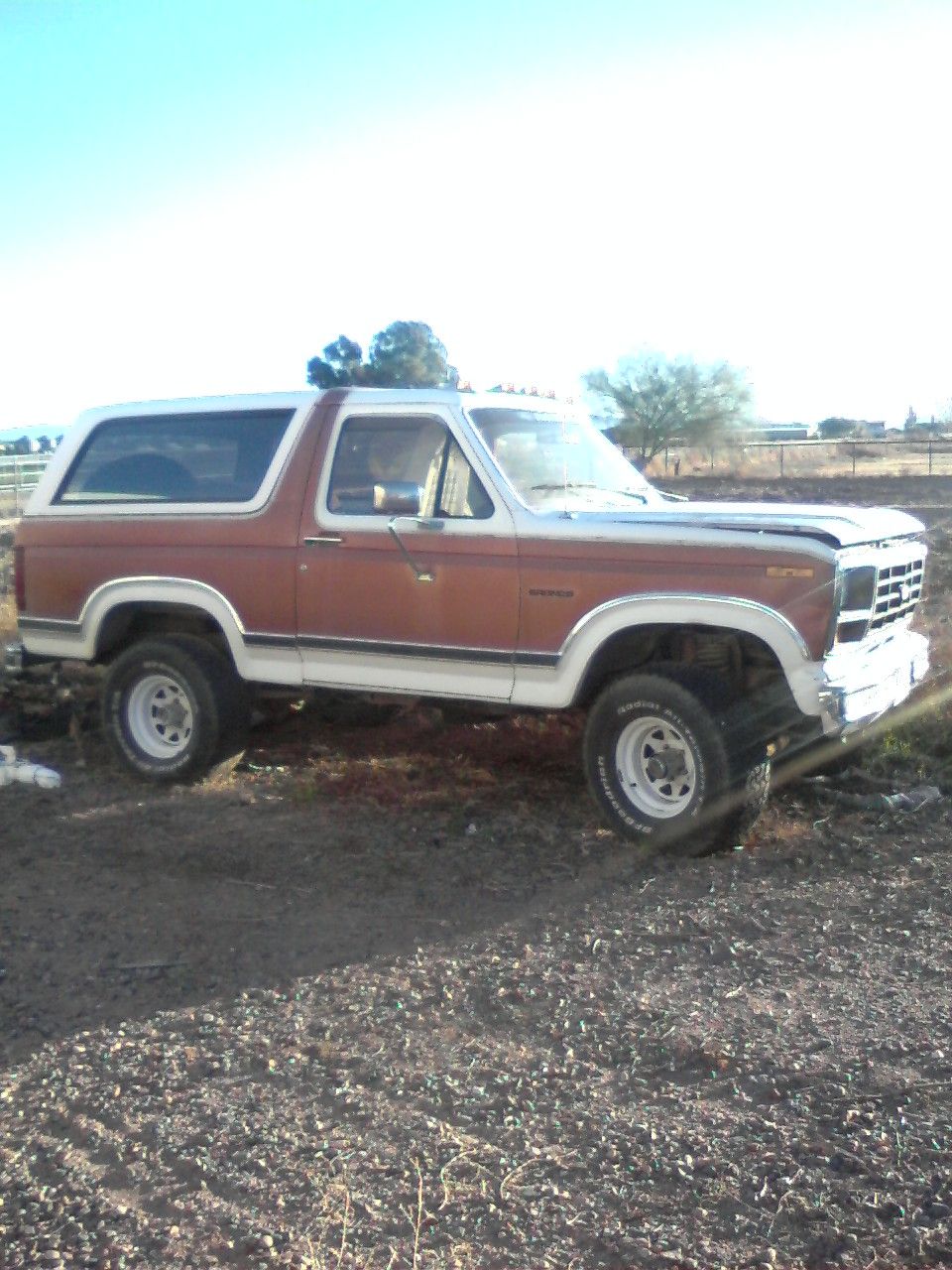 Two-tone red and white full-size SUV parked on dirt in a rural field