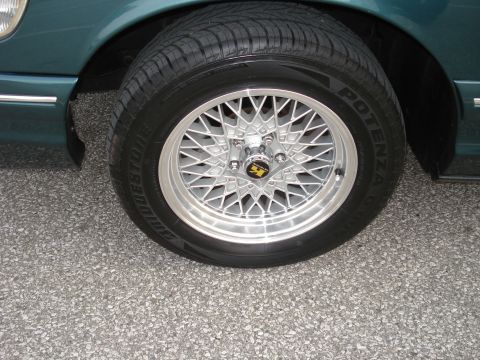 2000 Ford Crown Victoria - A close-up view of a car's wheel and tire, a silver mesh design and a yellow center cap emblem.