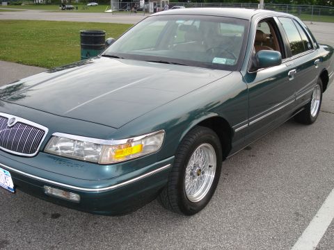 2000 Ford Crown Victoria - Green Mercury Grand Marquis from the front-right quarter, showing wire wheels and a chrome grille.