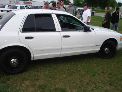 2000 Ford Crown Victoria - Side view of a white 2000 Ford Crown Victoria with people gathered around it.
