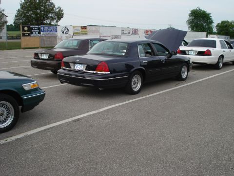 2000 Ford Crown Victoria - Several Ford Crown Victorias are parked in a lot, with one having its hood open.