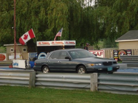 2000 Ford Crown Victoria - A 2000 Ford Crown Victoria is seen on a drag strip with flags in the background.